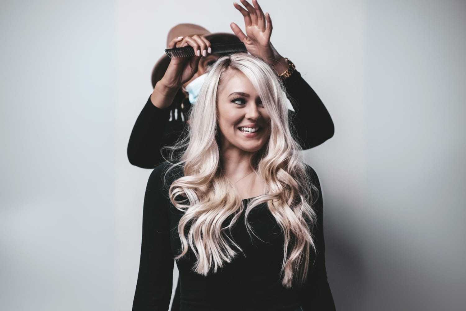 Stylist adjusting a woman's long, blonde hair in a salon setting.