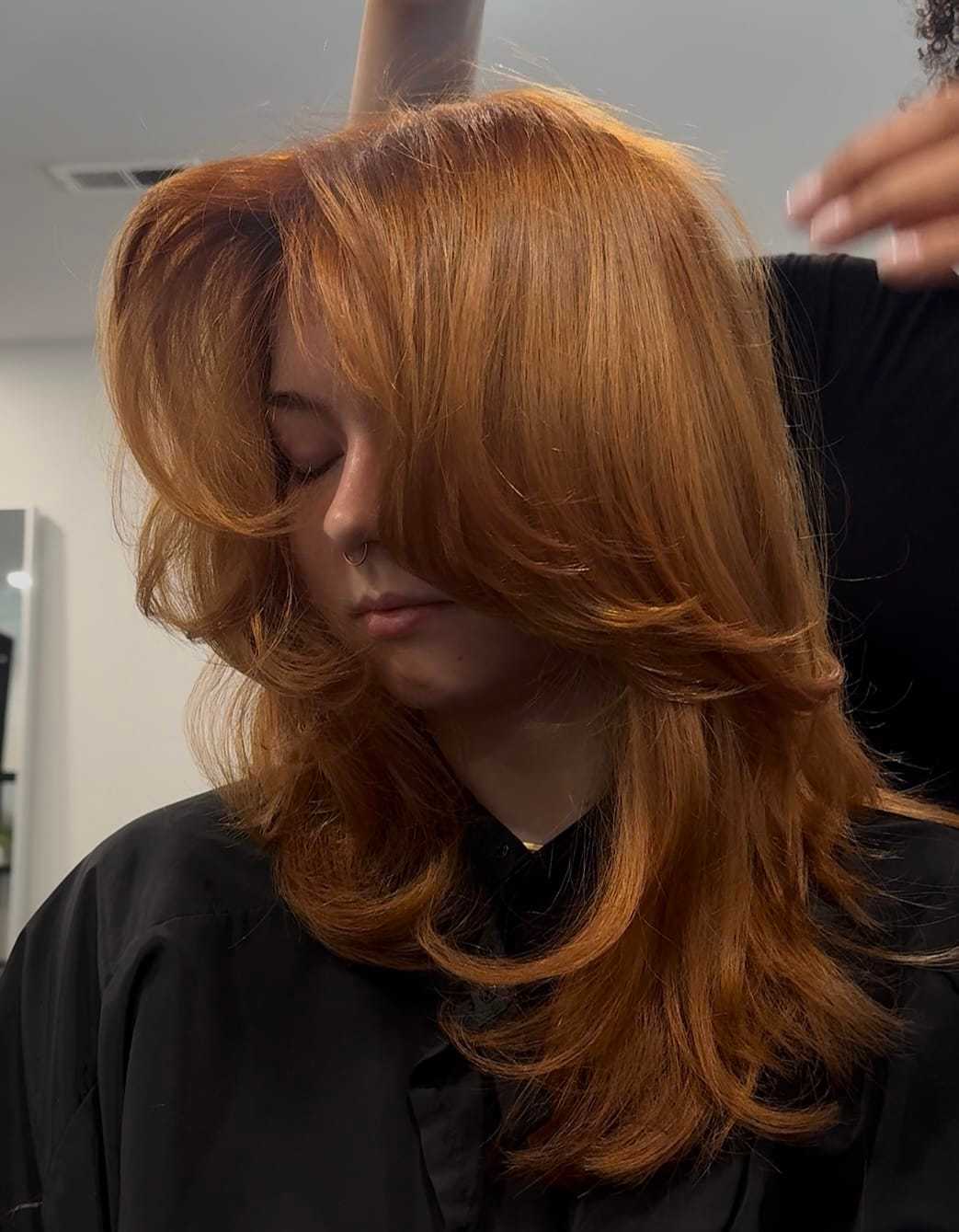 Person with layered auburn hair getting a trim at a salon.